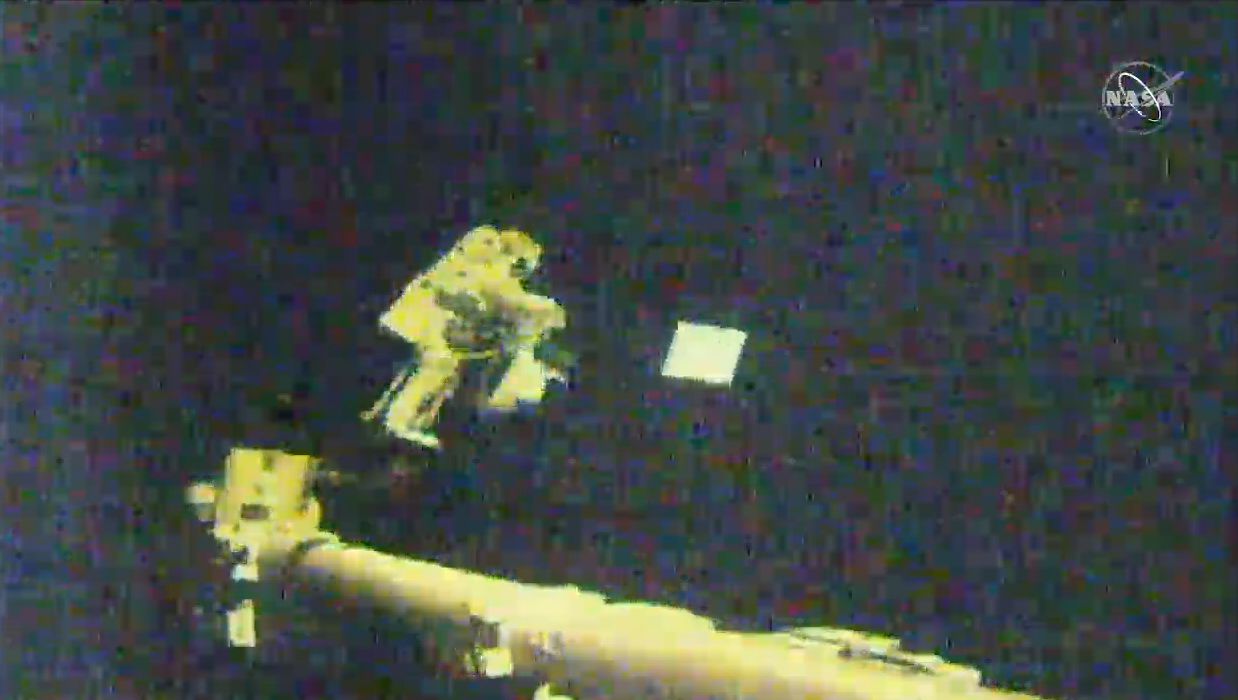 Astronaut Victor Glover tosses an antenna cover into space for disposal while riding a robotic arm outside the International Space Station during a spacewalk on Jan. 27, 2021.