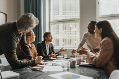 A team of smiling business professionals discuss ideas while sitting around a table in a meeting room