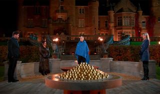 four people (l-r, Chris C.T. Tamburello, Mercedes "MJ" Javid, Alan Cumming, and Trishelle Cannatella) stand around a table of gold coins in a castle garden, in season 2 of 'the traitors'