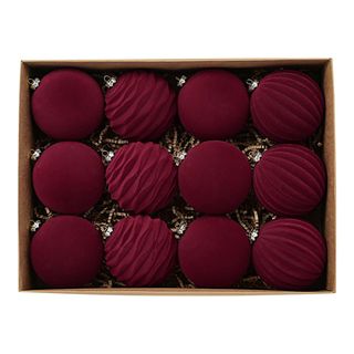 12 deep red velvet Christmas baubles in a brown cardboard box, resting on shredded packing paper