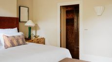 neutral bedroom with a dark red headboard, white sheets, a patchwork throw pillow, burl wood side table and a shell wall sconce