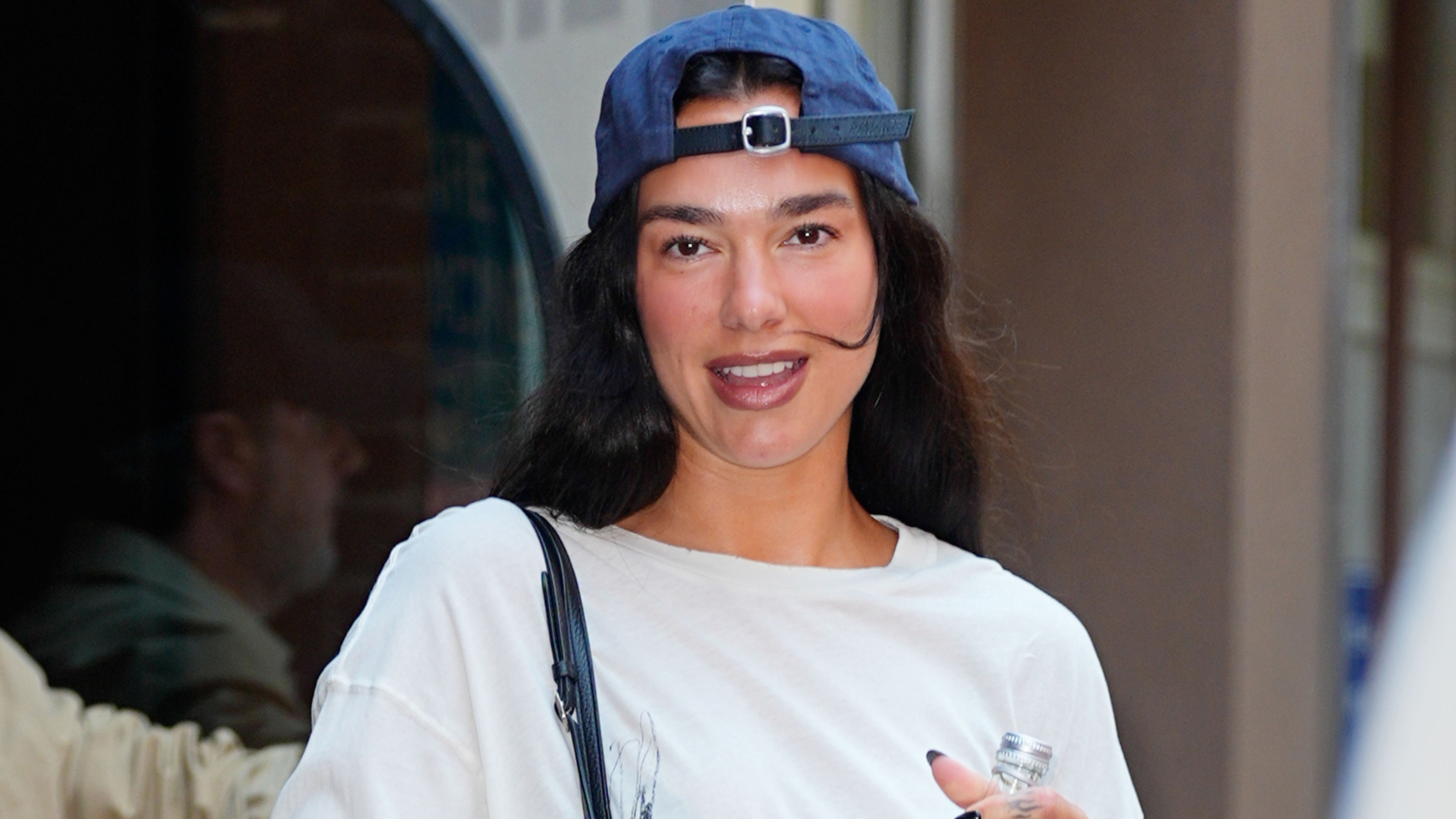 Dua Lipa wearing a white tee, jean shorts, ballet flats, and a baseball cap 
