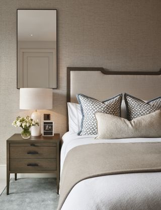 neutral bedroom with wallpaper, mirror, patterned pillows, taupe blanket, teal accents