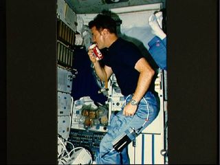Astronaut Anthony W. England, mission specialist, drinks from a special carbonated beverage dispenser labeled Coke while floating in the middeck area of the shuttle Challenger during the STS-51F mission in 1985. Note the can appears to have its own built in straw.