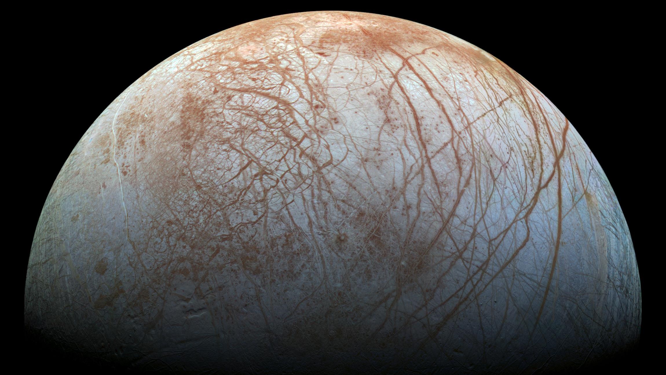 The surface of Europa shows linear cracks and ridges across the surface