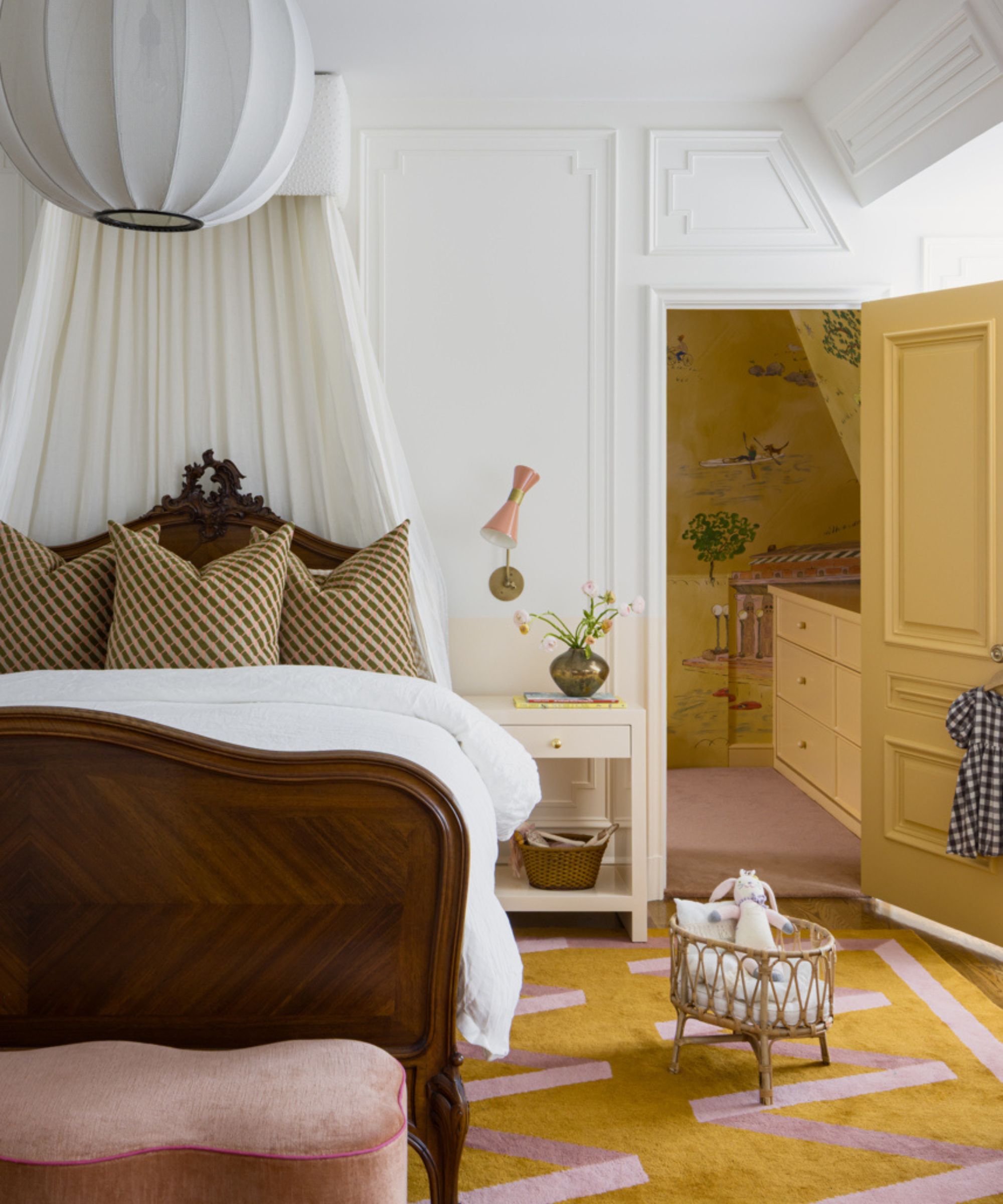 sophisticated bedroom with wooden traditional bed with white canopy, pink footstool, mustard yellow and pink rug and yellow door