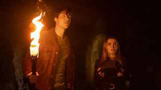 Drake Rodger as John Winchester and Meg Donnelly as Mary Campbell walking with a torch in The Winchesters season 1
