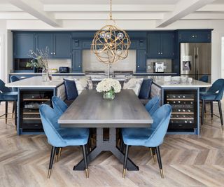 large kitchen with U shaped island, central dining table inbetween and blue velvet chairs