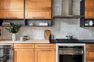 wooden kitchen with white textured tiles and stainless steel oven and wine fridge