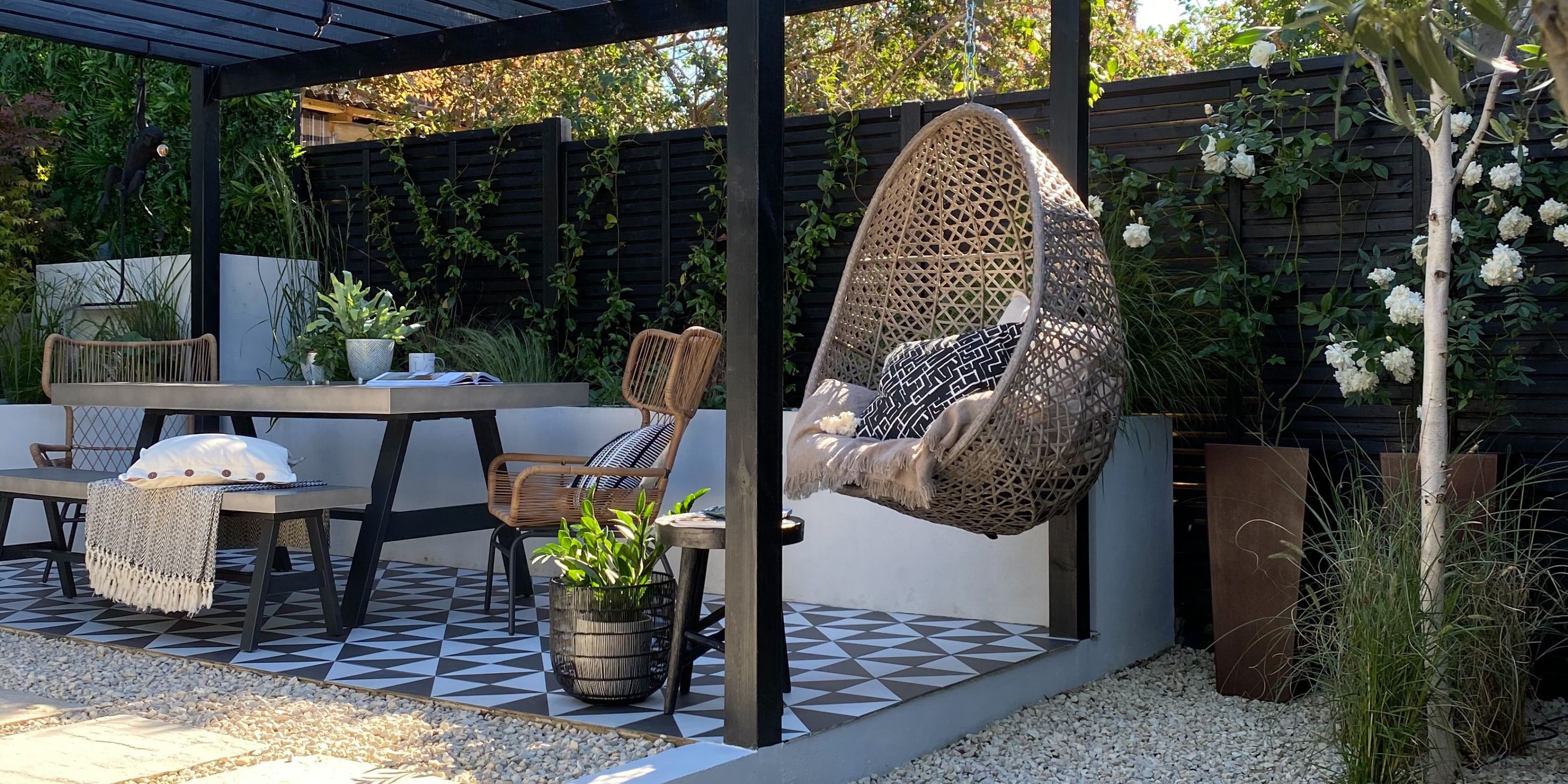 A raised outdoor seating zone with black and white tiled floor, hanging seating and a pergola