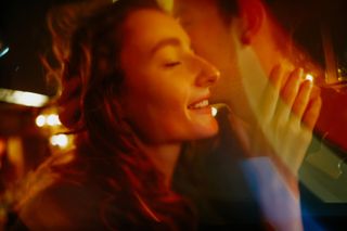 Young happy girl in the bright multicolor lights is smiling and looking away. She hugs her boyfriend gently. Only his chin and neck are seen.