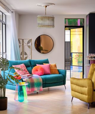 A white living room with a circular mirror on the wall, a blue couch with colorful throw pillows, and a yellow chair
