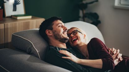 Happy couple lying together on sofa in living room at home