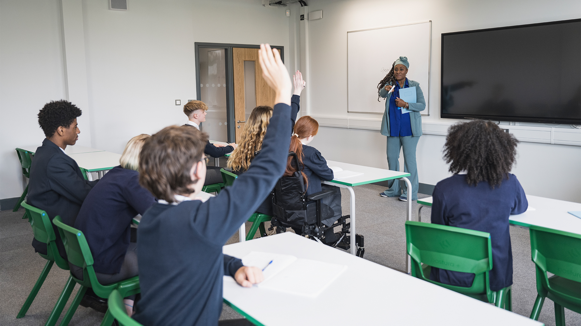 British high school kids in a classroom with teacher speaking to pupils.