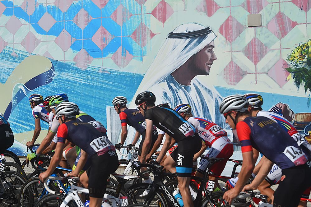 The peloton passes a mural Abu Dhabi Tour