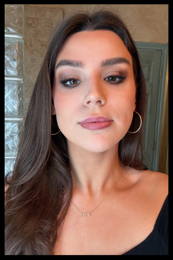 a girl with long dark hair, eye makeup, and gold hoop earrings in a black top