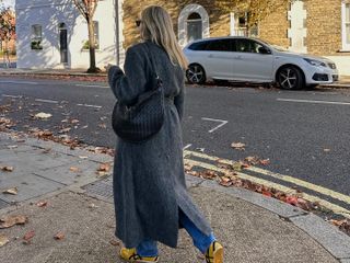 Fashion influencer Lucy Williams on the street wearing a long grey winter coat, blue jeans, and yellow sneakers with a Bottega Veneta bag.