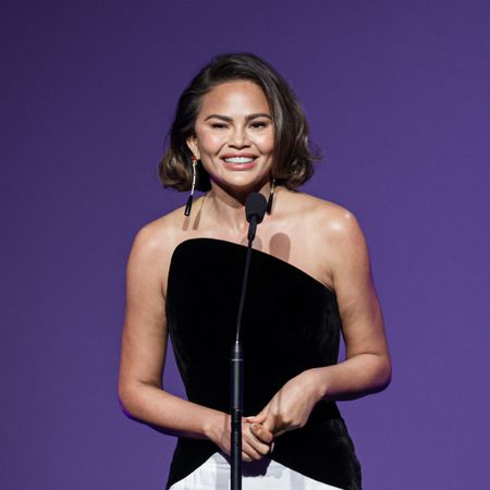 chrissy teigen speaks on stage wearing a black and white gown