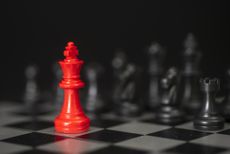 Red King chess piece with the other pieces in black blurred in the background