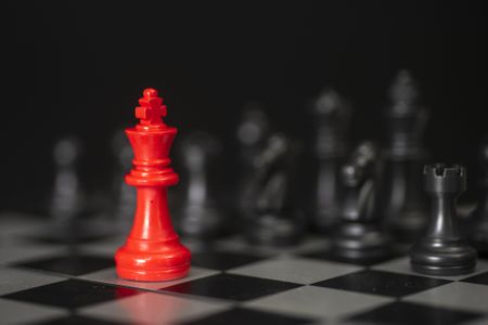 Red King chess piece with the other pieces in black blurred in the background