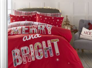 A bedroom with red slogan 'Merry and bright' bedding set and grey button-backed upholstered armchair
