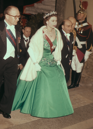 Queen Elizabeth II, wearing the red sash of the Legion Of Honour over her dress, arrives for a state banquet at the Louvre museum with French politician Guy Mollet, on April 11th 1957