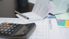 Financial paperwork scattered over a desk along with a calculator and pen.