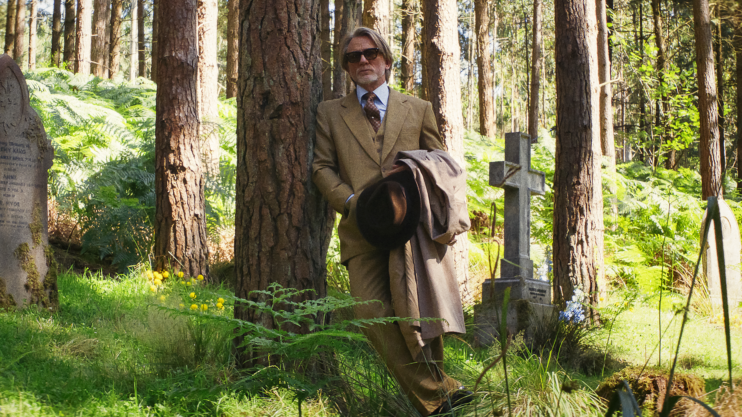 Benoit Blanc (Daniel Craig) leans against a tree in a graveyard in &quot;Wake Up Dead Man: A Knives Out Mystery&quot;
