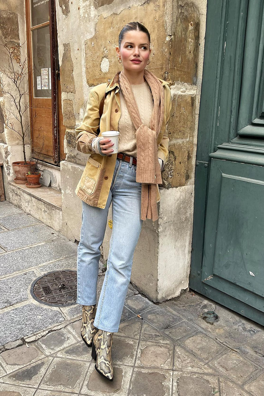 A woman wearing a knit sweater, corduroy jacket, blue jeans, and snakeskin boots