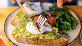 Person eating avocado and poached eggs on toast