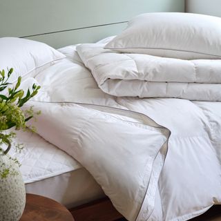 Pile of plain duvets and pillows with a sage green wall in the background