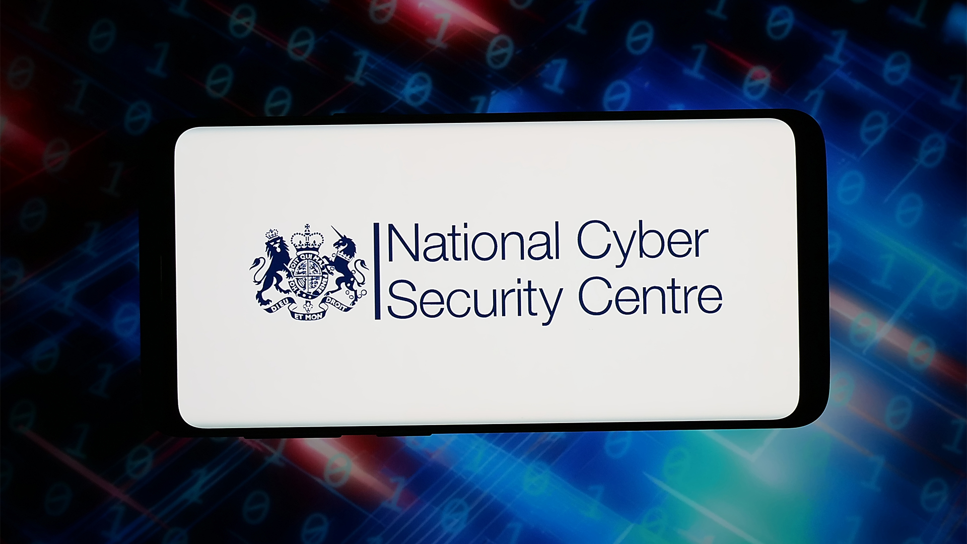 Insignia of the UK's National Cyber Security Centre (NCSC) pictured on a smartphone screen with blurred blue, green, and orange coloring in background.