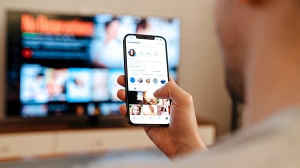 Young man looking at phone and TV