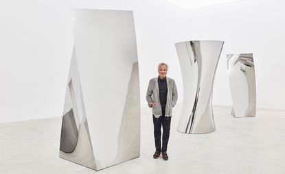 British sculptor Anish Kapoor, pictured with his sculptures at his ’Gathering Clouds’ exhibition at Kukje Gallery in Seoul. A man standing between 3 large silver objects with different shapes..