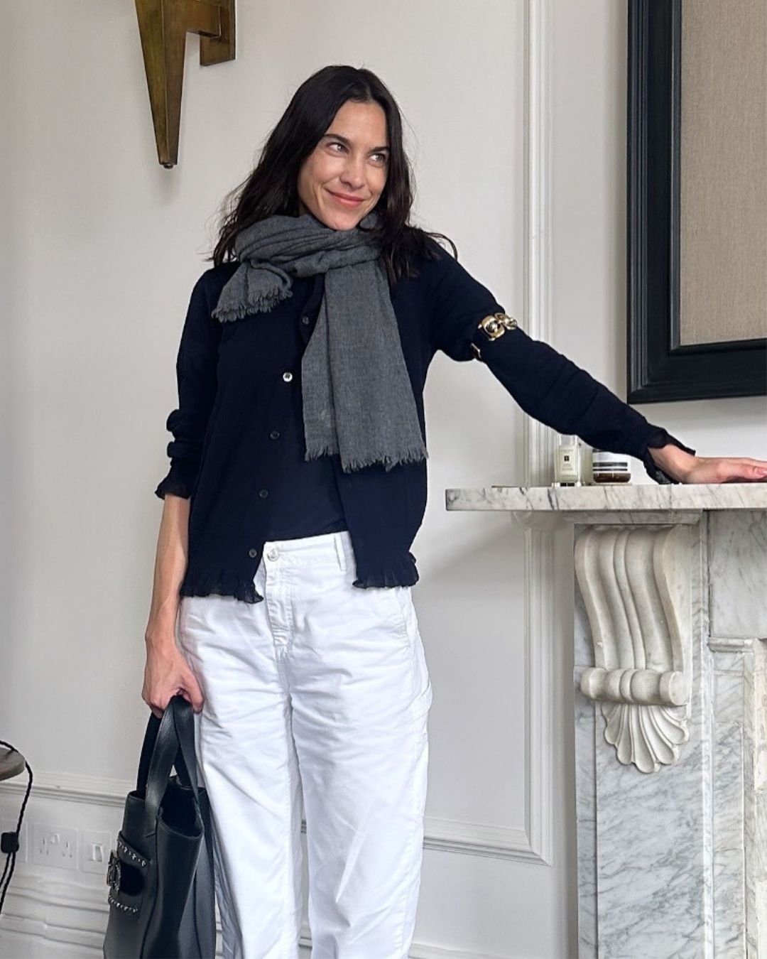 Alexa Chung wears white jeans with a navy cardigan and grey scarf.