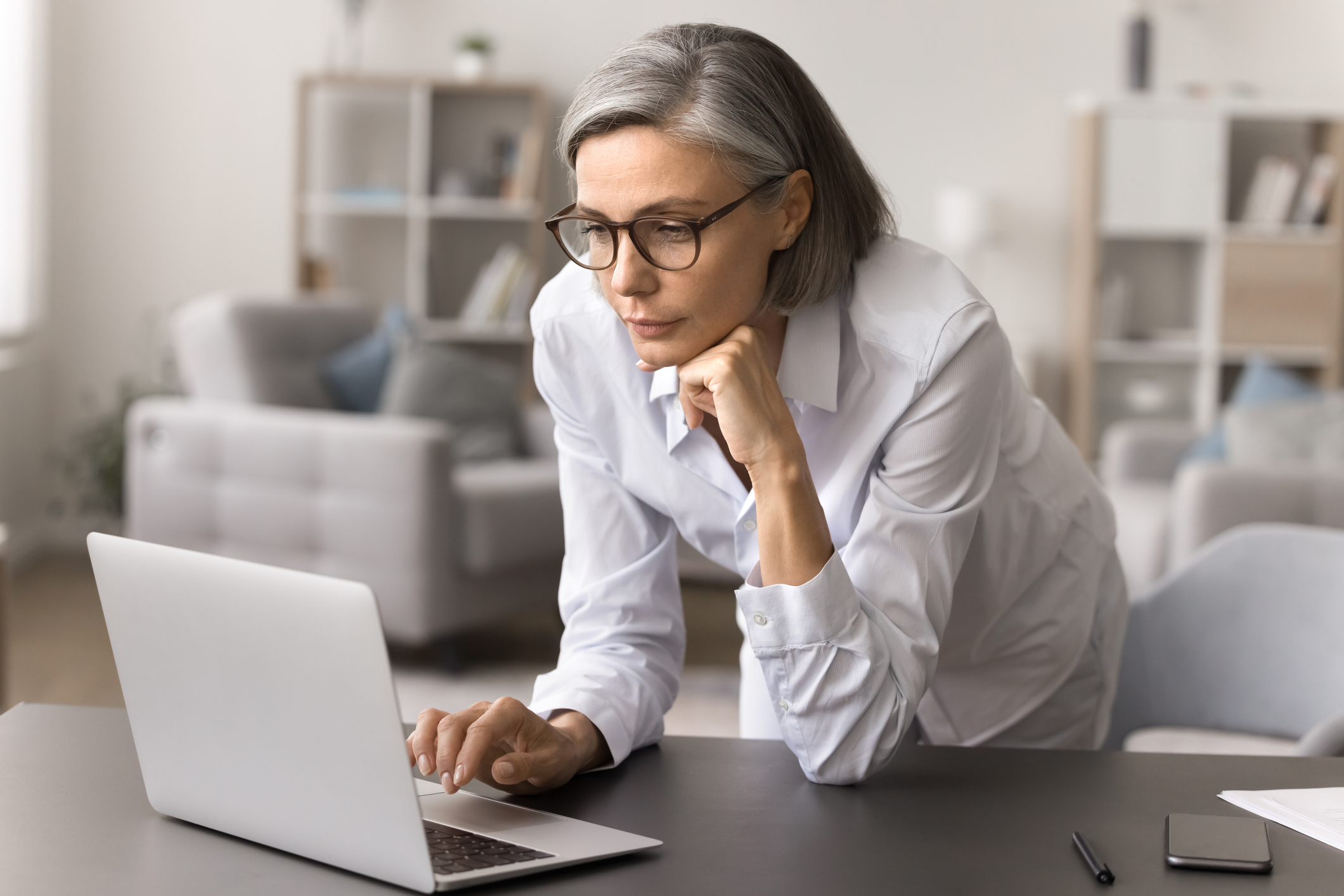 Focused mature businesswoman learn new commercial offer, read business news in e-mail leaned at workplace desk, using laptop for freelance, review sales results, engaged in brainstorm at home office.