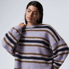 Young woman wearing a purple knitted jumper with blue, brown, and white stripes 