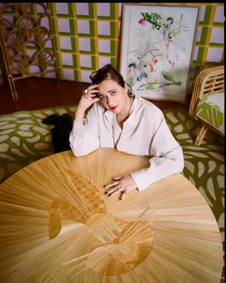 A woman dressed in a white blouse sits at a wooden table decorated with a rabbit motif in an imaginative and colorful room.