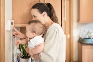 mother holding baby and pointing at thermostat at home
