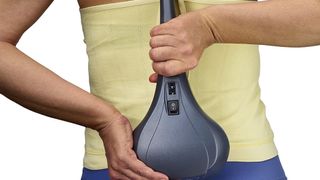 Thumper Sport Percussive review: A woman uses it to massage her lower back after exercise