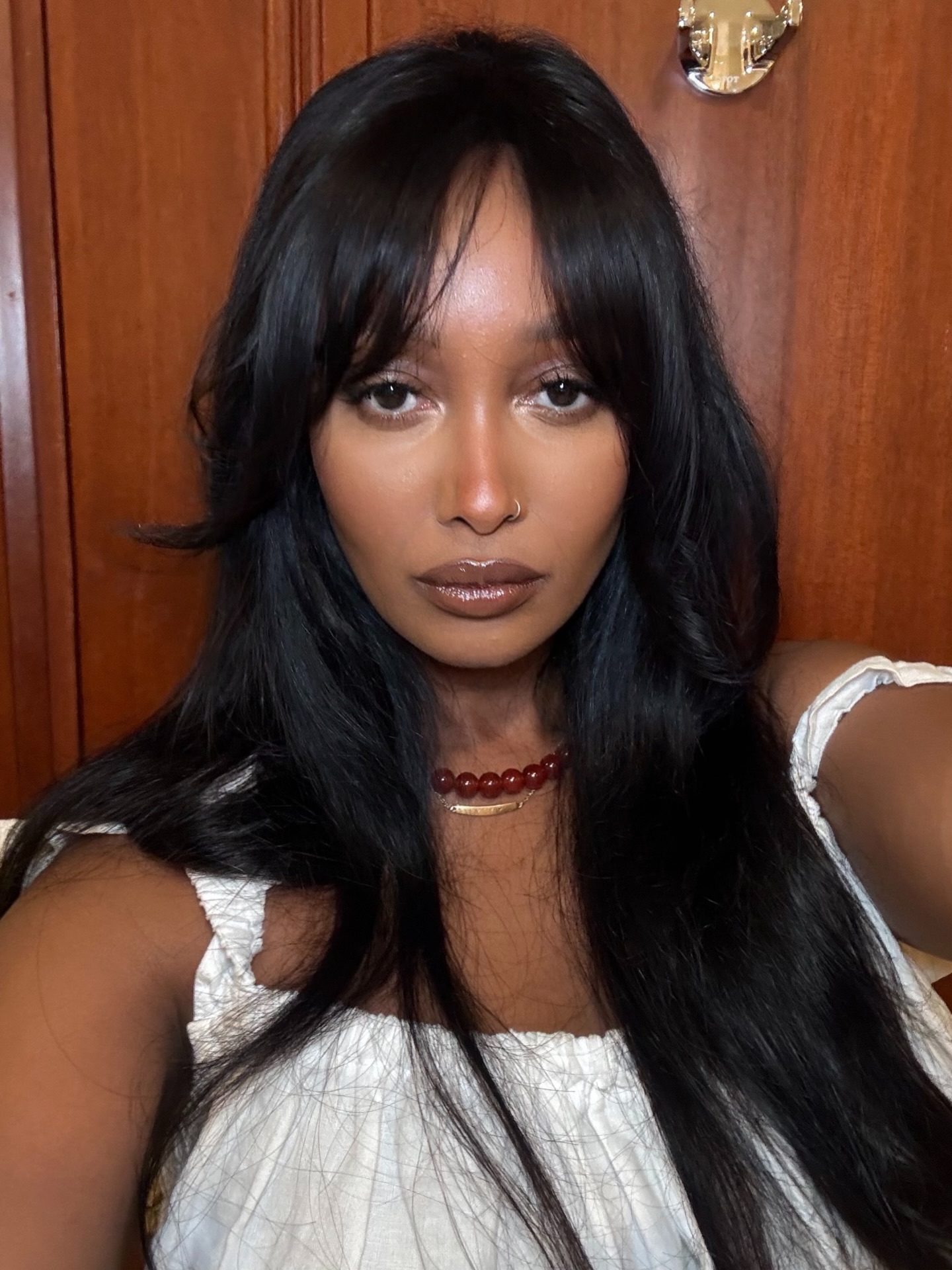 Mona M. Ali with a bronzed complexion, brown lips, and and curtain bangs