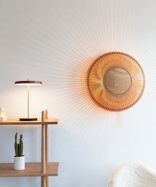 white wall with starburst effect wall light and small console table with contemporary table lamp