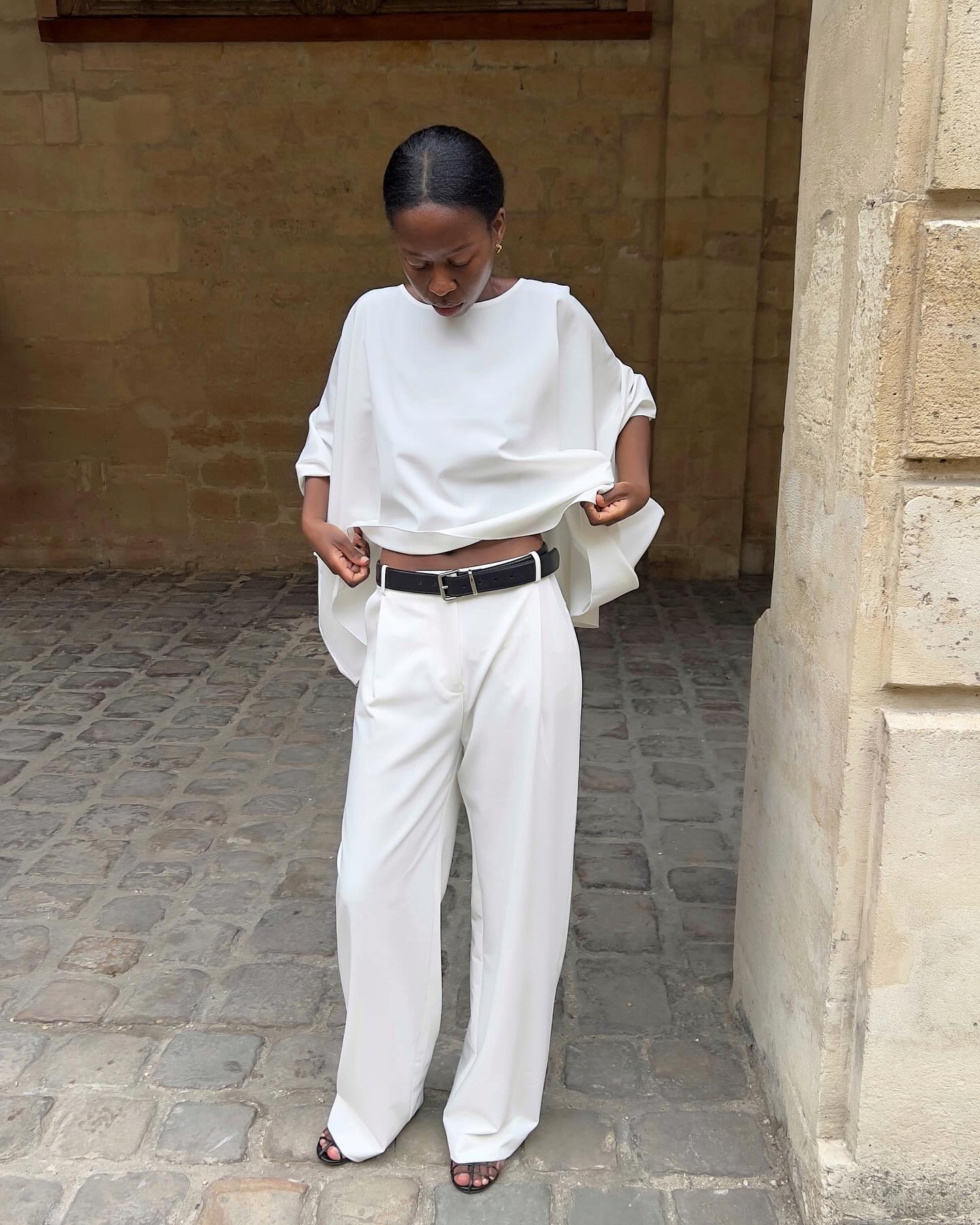 Woman wearing a white cape top and white trousers.