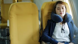 A woman with dark hair sleeps on a plane with yellow seats as a way to avoid jet lag and get over it quickly if she does experience it