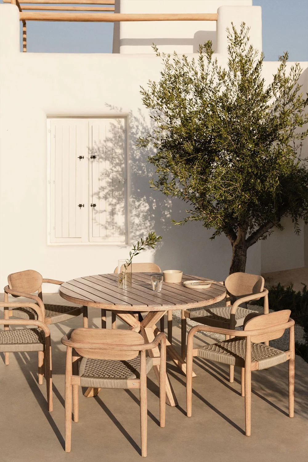 round outdoor dining set on a patio with a large potted olive tree