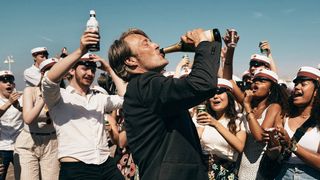 Mads Mikkelsen drinks out of a bottle in front of a crowd in Another Round
