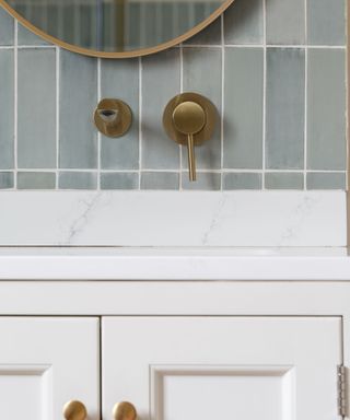 A close-up of a white bathroom sink with gold faucets and handles on it and above it and light blue tiles