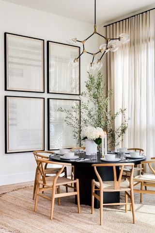 dining room apartment with round black table, wood chairs, coir rug, artwork, glass pendant, drapes