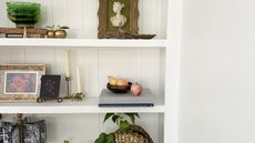 A set of white shelves displaying an array of decor and accessories including photo frames, candlesticks, and books