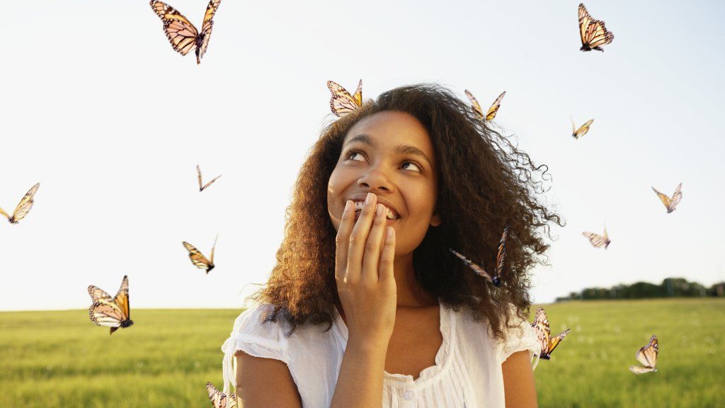 A woman holds her hand over her mouth and looks at flying monarch butterflies